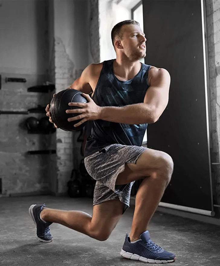 Man doing a lunge while holding a medicine ball in a training studio